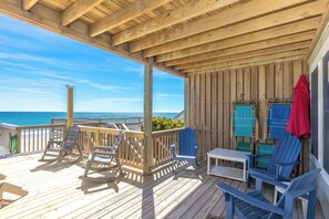 A wooden deck with a view of the ocean, outdoor furniture, and a covered area with a table and chairs.