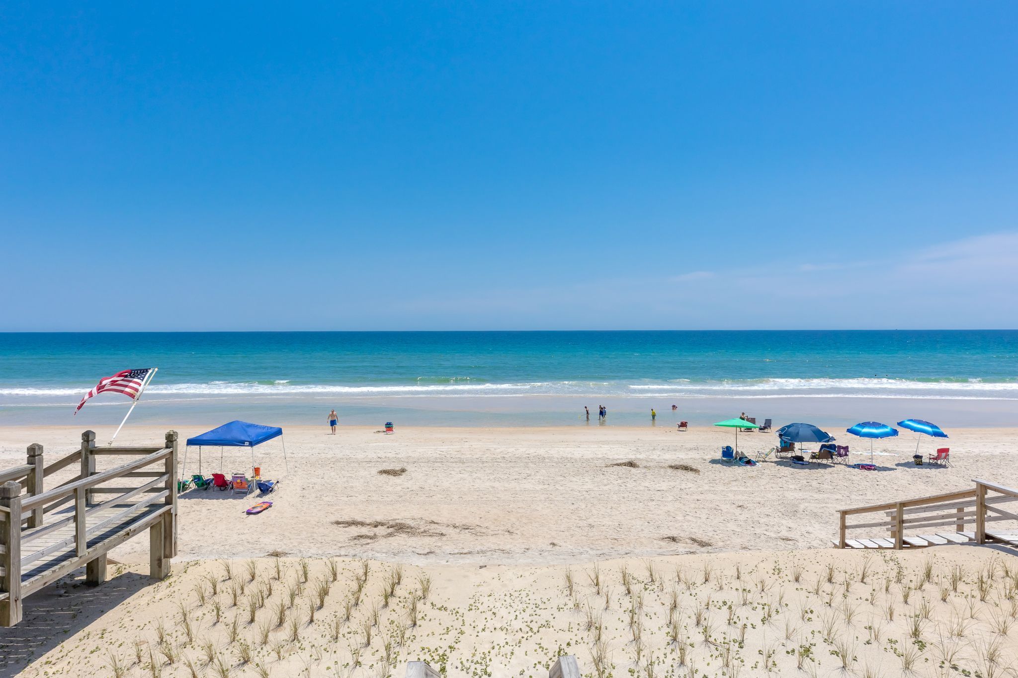 Een strand met een houten looppad, ligstoelen, parasols en een vlag.