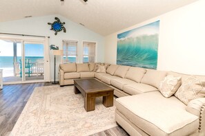 A living room with a large sectional sofa, a coffee table, and a painting of a wave.