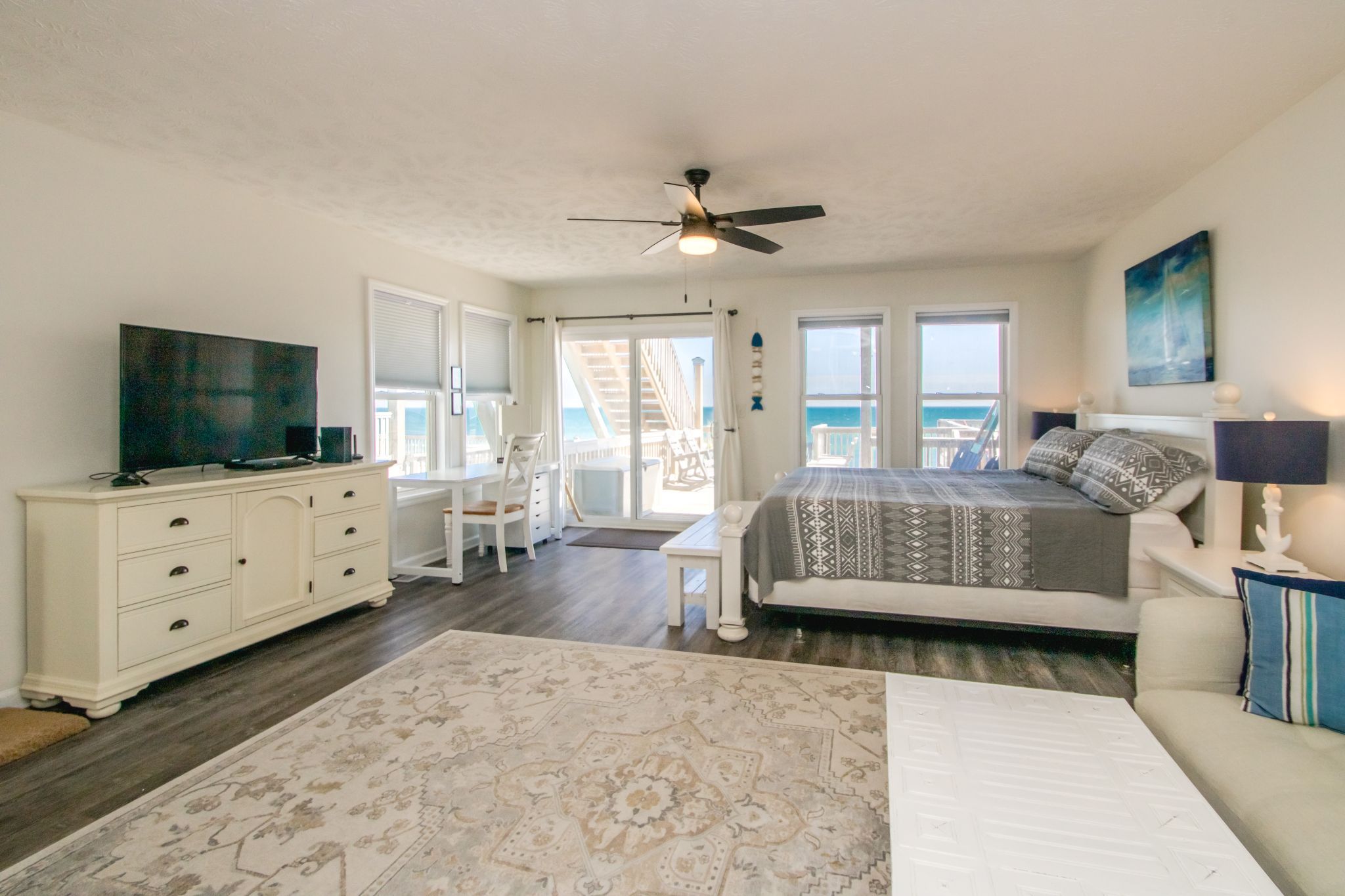 A bedroom with a bed, dresser, TV, and a view of the ocean.