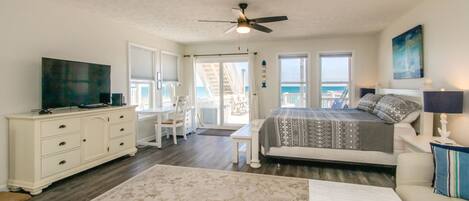 A bedroom with a bed, dresser, TV, and a view of the ocean.