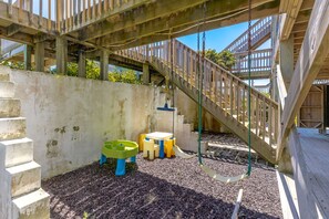 A wooden deck with a swing set, a small table, and a slide.