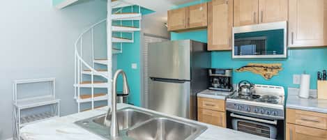 Una cocina con un lavamanos de acero inoxidable, un refrigerador, una estufa y un microondas.