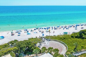 A beach with numerous umbrellas and sun loungers, a clear blue sea, and a circular viewing platform with a railing. - 30A Home-Close to Pool-Golf Cart-Close 2 Beach (Santa Rosa Beach)