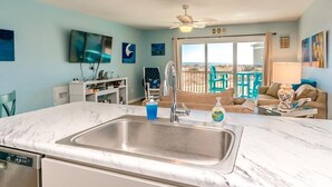 A kitchen with a marble countertop, stainless steel sink, and a ceiling fan. - 715 Surf - Gorgeous 1BR Surf Condo with Washer and Dryer (Surf City)