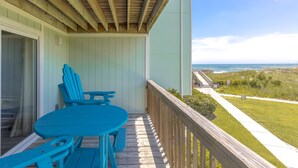 A wooden deck with a table and chairs, overlooking a beach and ocean view. - 715 Surf - Gorgeous 1BR Surf Condo with Washer and Dryer (Surf City)