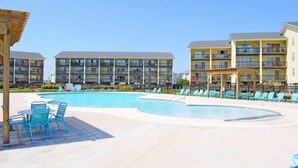 A resort with a swimming pool, lounge chairs, and multi-story buildings with balconies. - 715 Surf - Gorgeous 1BR Surf Condo with Washer and Dryer (Surf City)