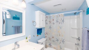 A bathroom with a white sink, a toilet, a shower with a starfish shower curtain, and a mirror with lights. - 715 Surf - Gorgeous 1BR Surf Condo with Washer and Dryer (Surf City)
