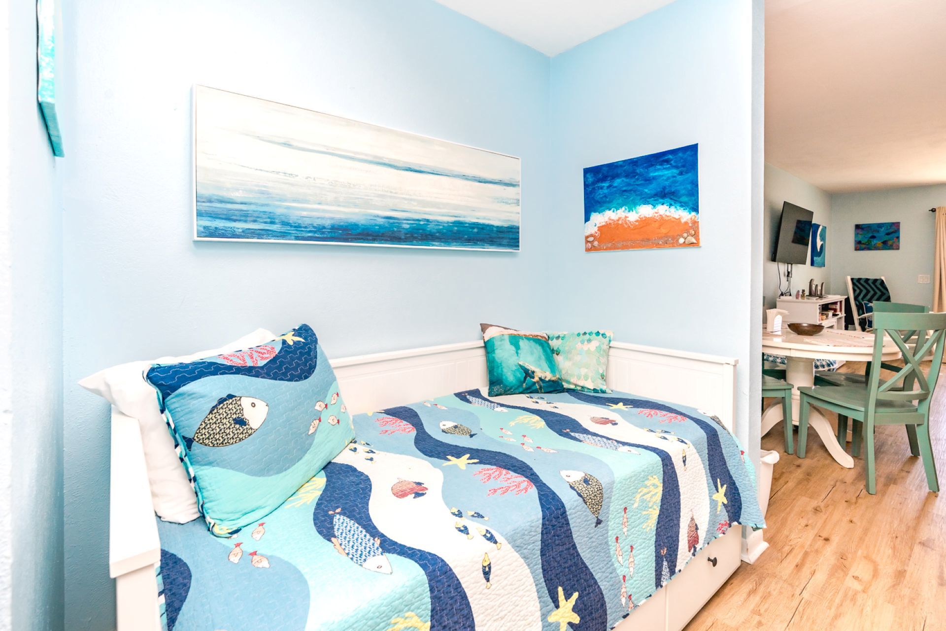 A bedroom with a bed, two pillows, a wall with two paintings, and a view into a dining area.