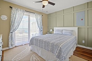 Une chambre à coucher avec un lit, des rideaux, un ventilateur de plafond, une horloge et une vue sur l’extérieur.
