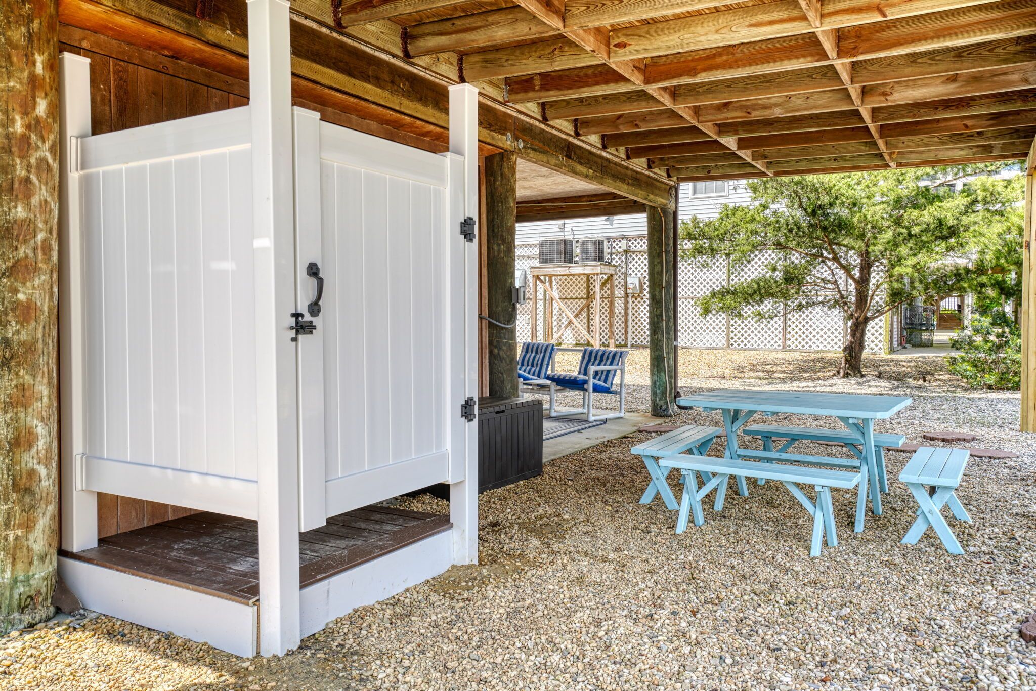 A covered outdoor area with a wooden ceiling, a white door, and a picnic table with benches.