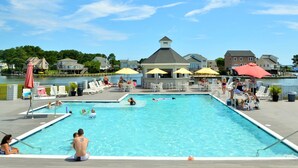Ein Schwimmbecken mit Liegestühlen und Sonnenschirmen, umgeben von Häusern und einem Gewässer.