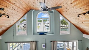 Ein Zimmer mit schräger Decke, einem Deckenventilator und einem großen Fenster mit einem Modell eines Segelboots.