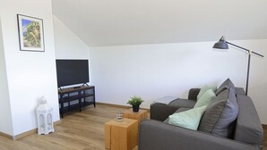 Ett modernt vardagsrum med en grå soffa, ett träbord, en tv på ett svart stativ, en vit lykta och en golvlampa.