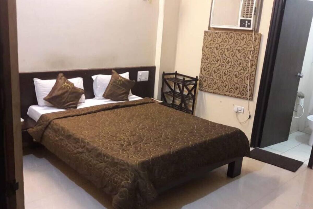A hotel room with a bed, pillows, a headboard, a wall-mounted air conditioner, a patterned wall, and a door leading to a bathroom.