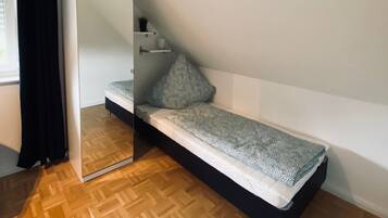 A small, modern bedroom with a loft bed, a mirror, and a small shelf with plants.