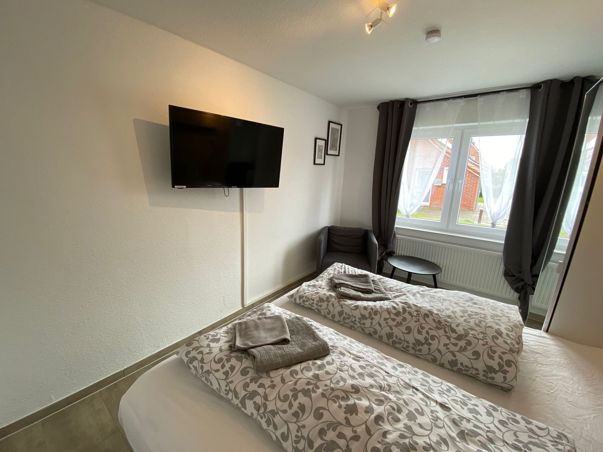 A hotel room with two beds, a TV mounted on the wall, a small table, and a window with curtains.