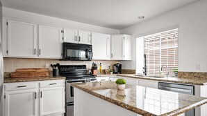 Una cocina moderna con armarios blancos, encimera de granito, microondas negro y cafetera.