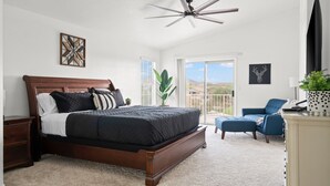 Un dormitorio con una cama grande, un ventilador de techo, una ventana con vistas al exterior y una silla azul.
