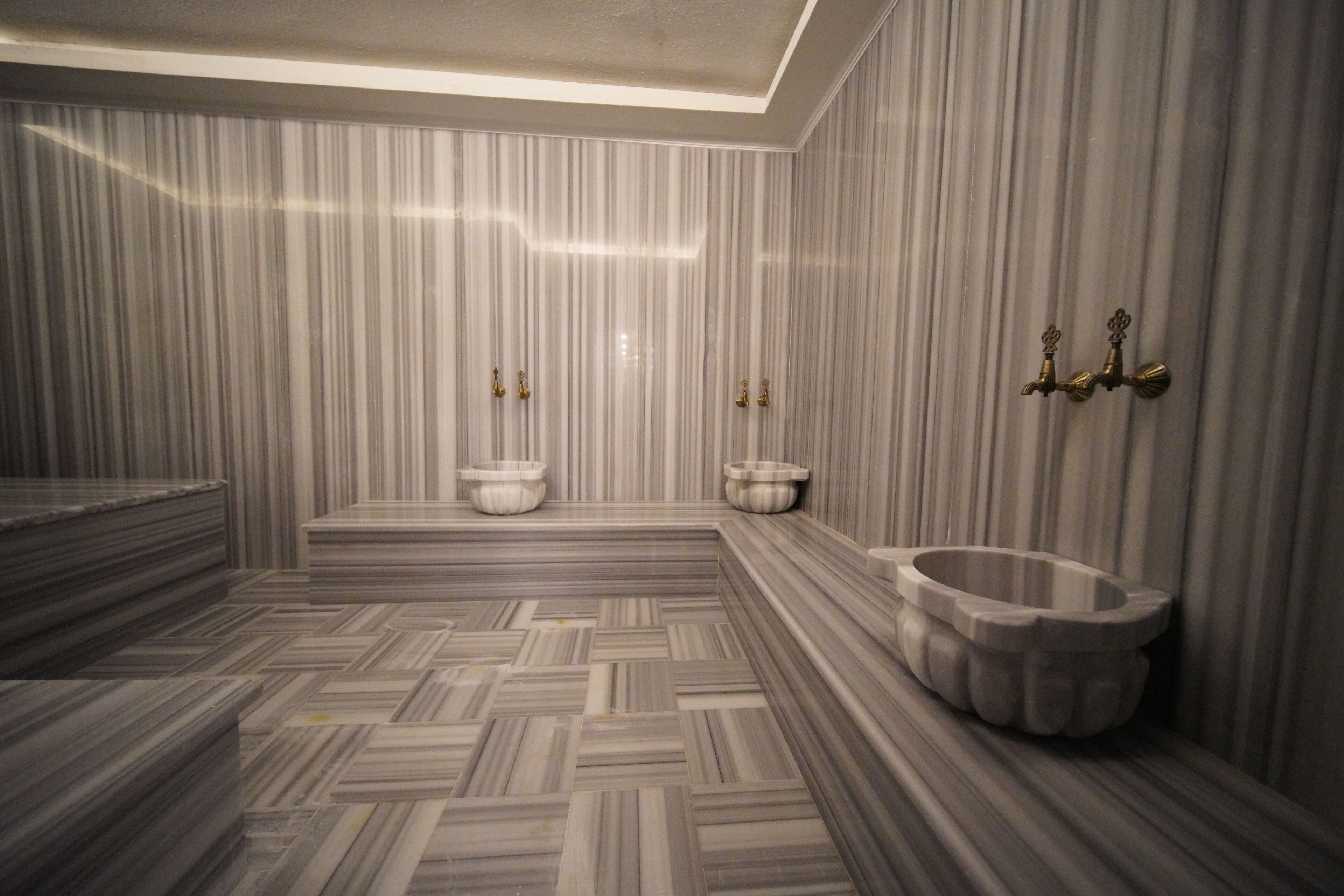 Une salle de bain avec un sol à motifs en chevrons, des murs en marbre et une baignoire sur pieds.
