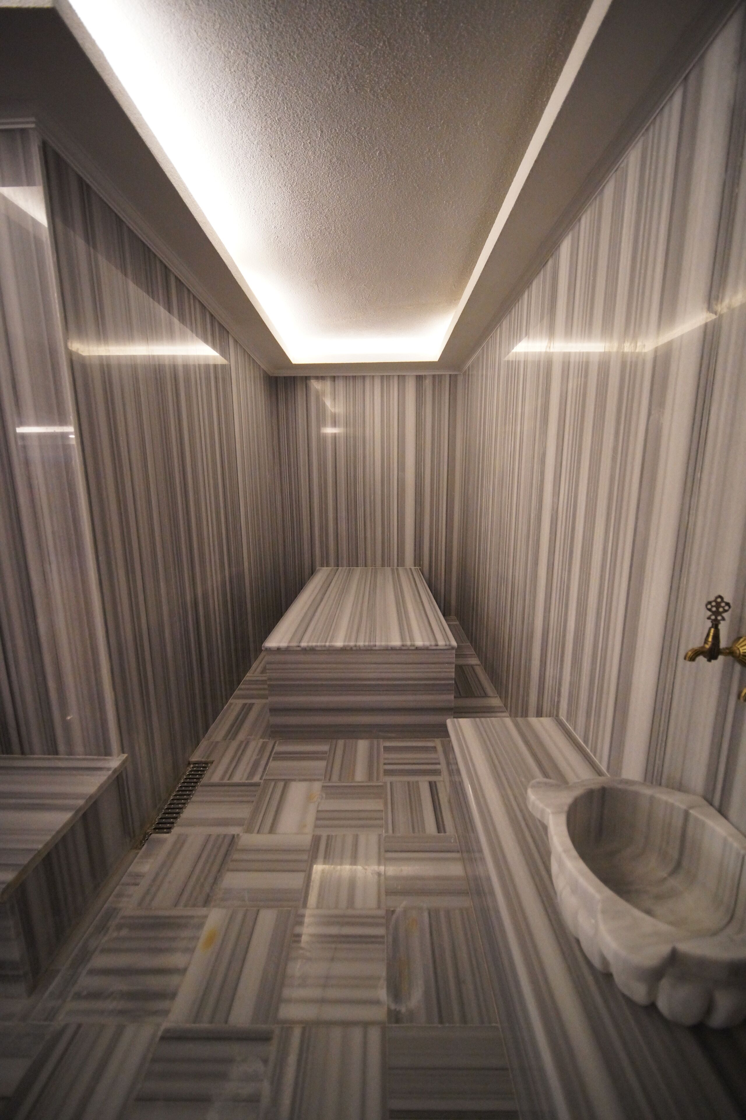Une salle de bain moderne avec des murs en marbre à rayures et un lavabo rectangulaire placé au centre.