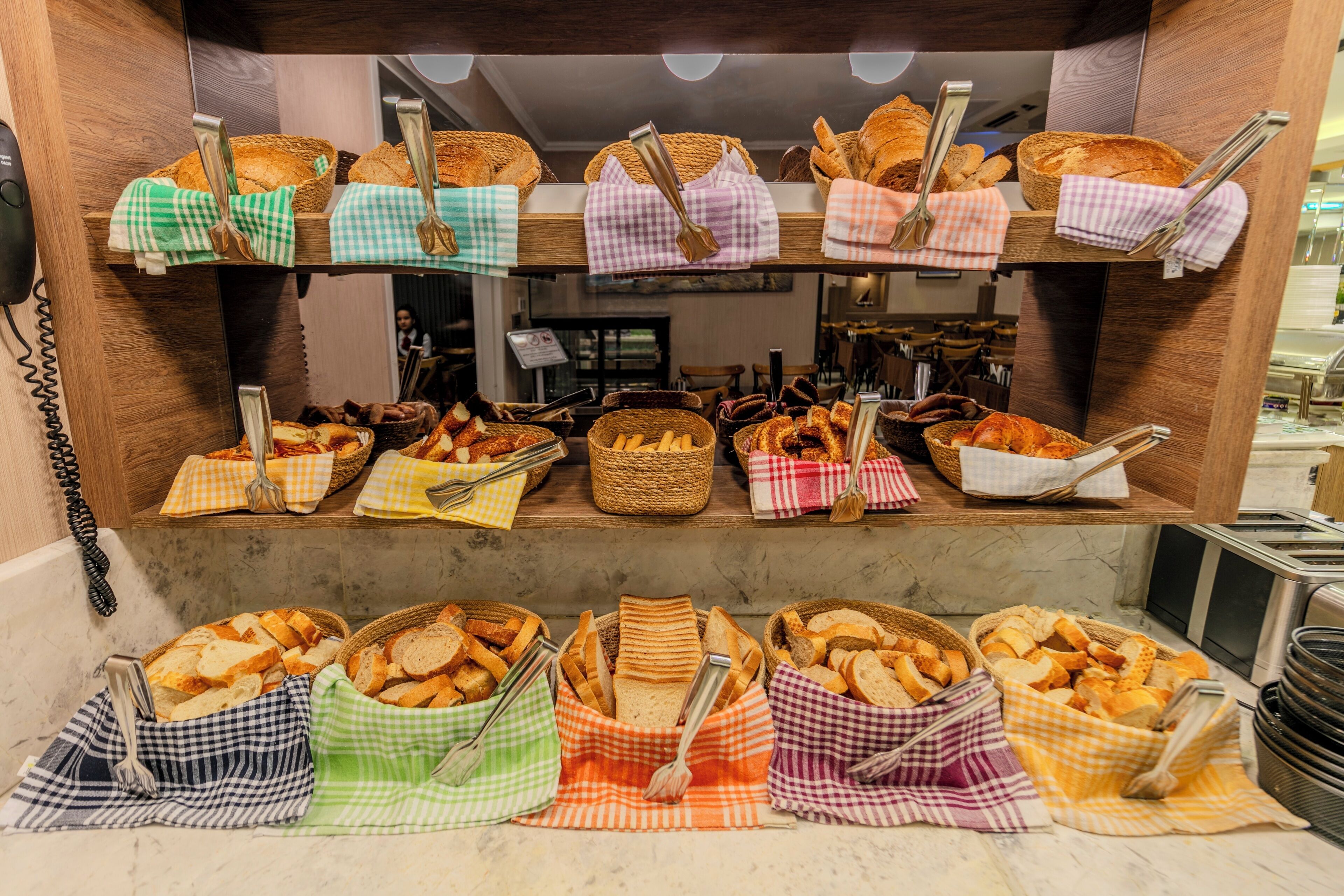A buffet with various breads and pastries displayed on shelves and in baskets, with serving utensils.