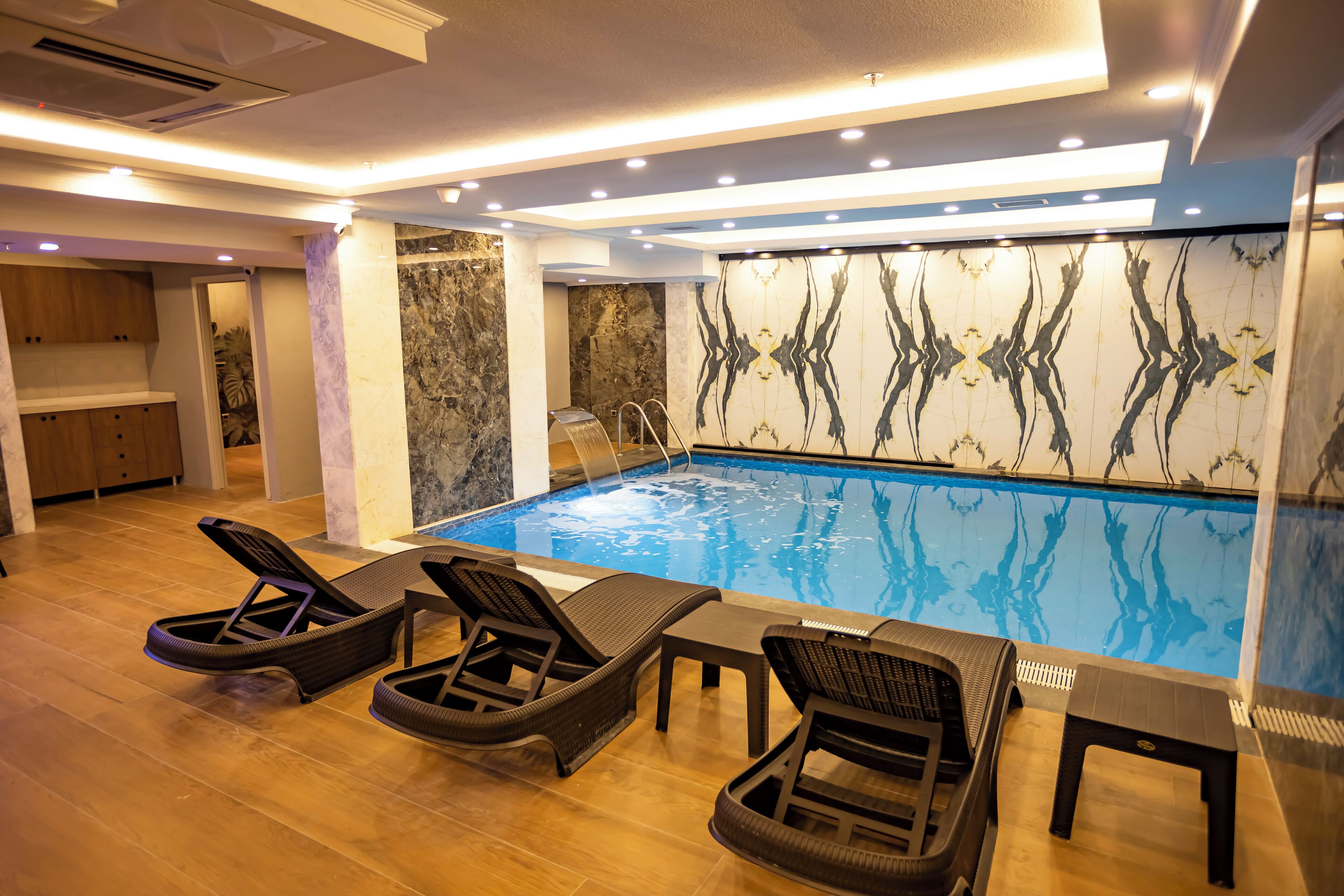 A modern indoor pool area with lounge chairs and a small table.