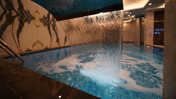A modern indoor pool with a water feature, clear blue tiles, and a marble wall with a tree design. - Hamitbey Hotel (Istanbul)