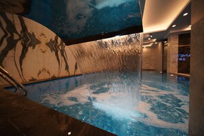 A modern indoor pool with a water feature, clear blue tiles, and a marble wall with a tree design. - Hamitbey Hotel (Istanbul)
