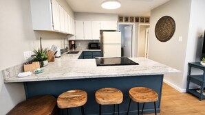 Une cuisine moderne avec des meubles blancs, un plan de travail en marbre, une cuisinière intégrée et un coin bar avec des tabourets.