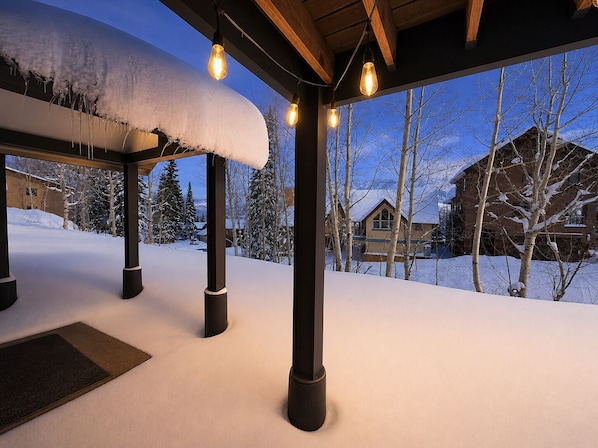 A snow-covered outdoor area with wooden beams and hanging lights, a wooden structure, and a view of snow-covered houses and trees. - Stylish Purgatory Ski Condo, Walk to Lifts (Durango)