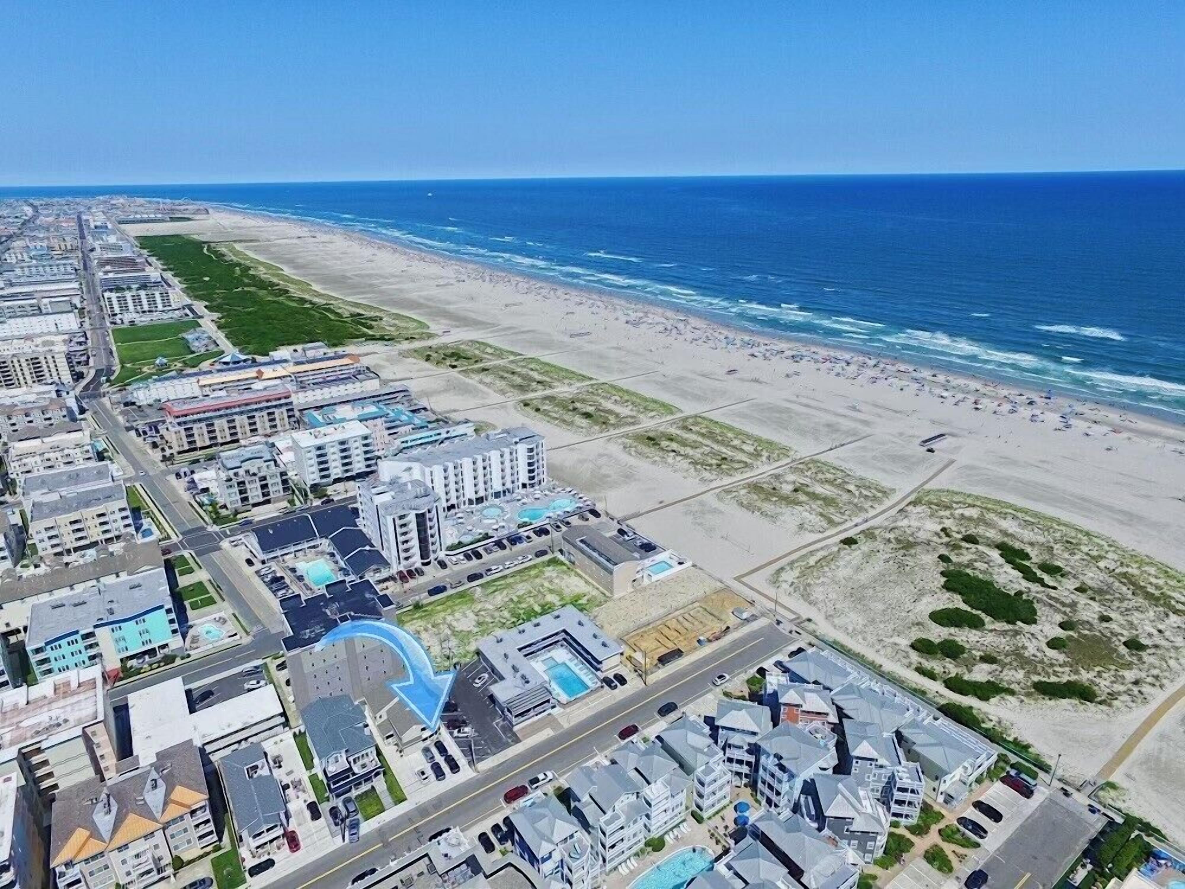An aerial view of a coastal area with buildings, a beach, and a clear blue sky.