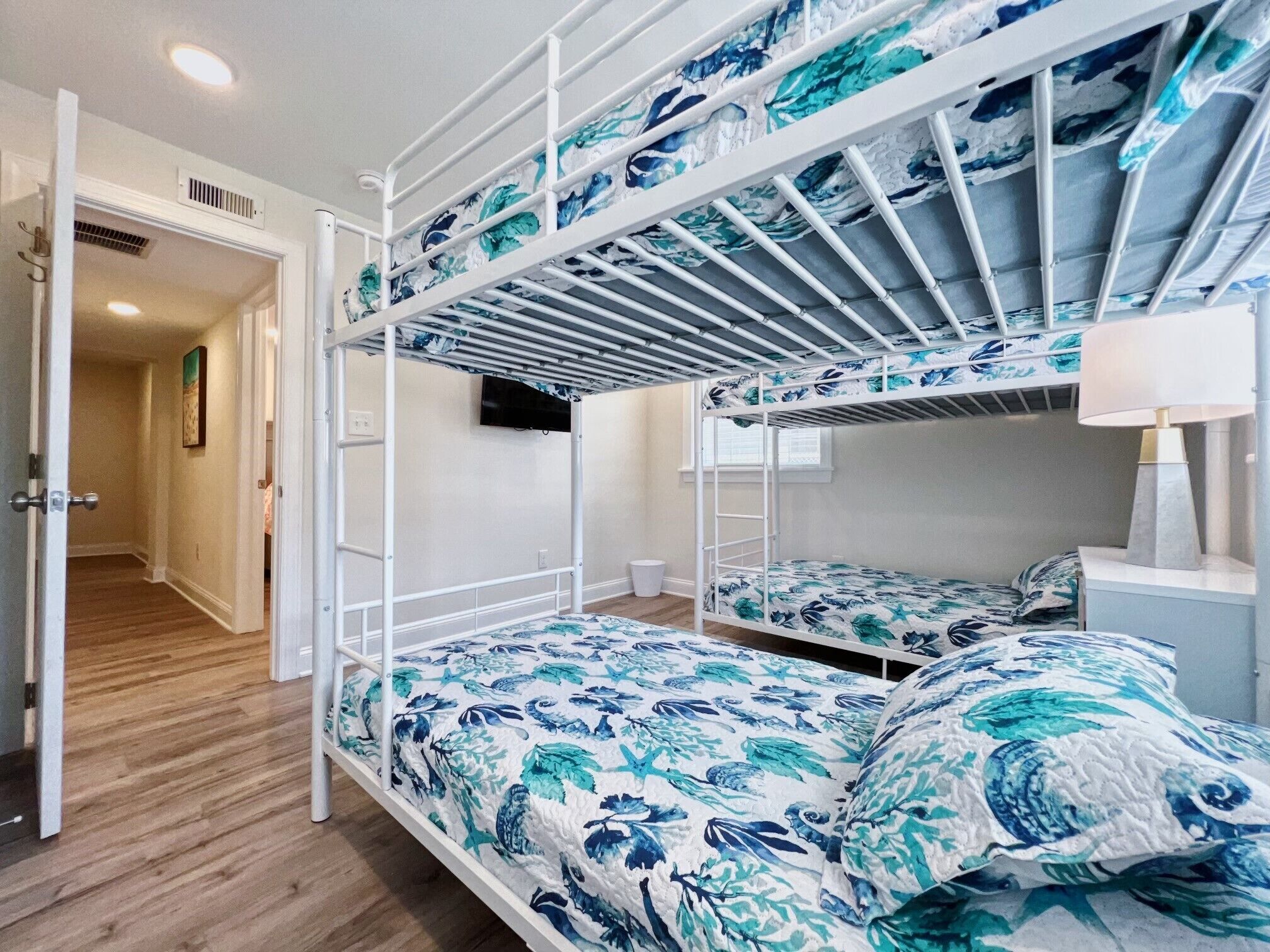 A bunk bed room with a wooden floor, a white door, and a wall-mounted TV.