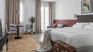A modern hotel room with a large bed, a desk with chairs, a potted plant, and a view of the city. - Bob W Madrid Atocha (Madrid)
