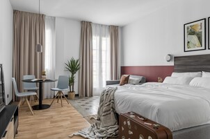 Ein modernes Hotelzimmer mit einem großen Bett, einem Schreibtisch mit Stühlen, einer Zimmerpflanze und Blick auf die Stadt.