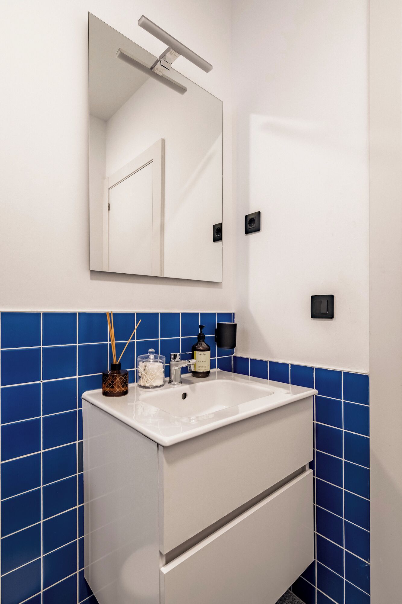 A bathroom with a white sink, blue-tiled walls, a mirror, and a door.