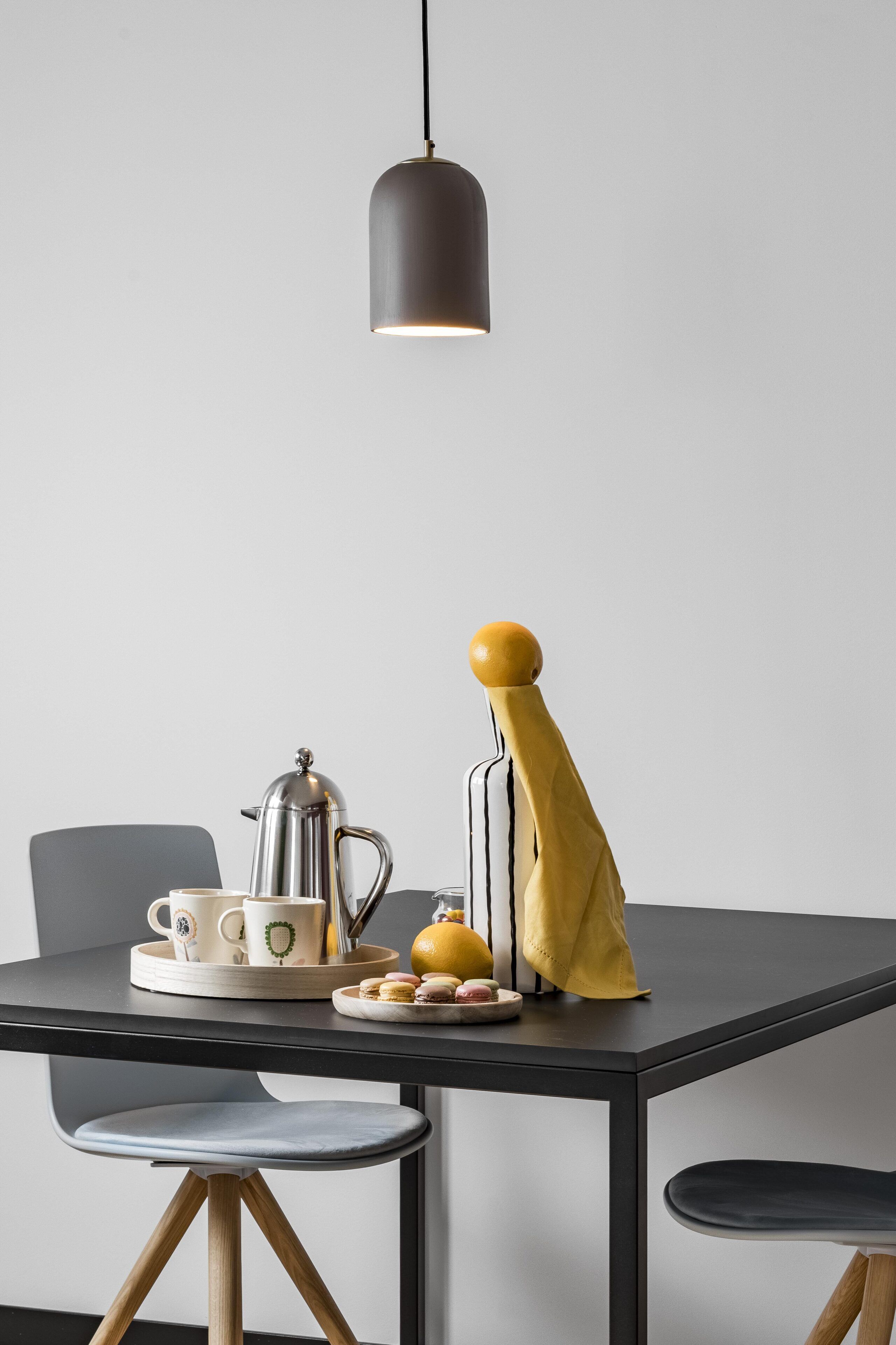 A modern dining area with a black table, two chairs, a coffee maker, cups, and a yellow cloth.