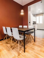 Ein moderner Essbereich mit Holztisch und weißen Stühlen, einer Pendelleuchte und einer Küche im Hintergrund.