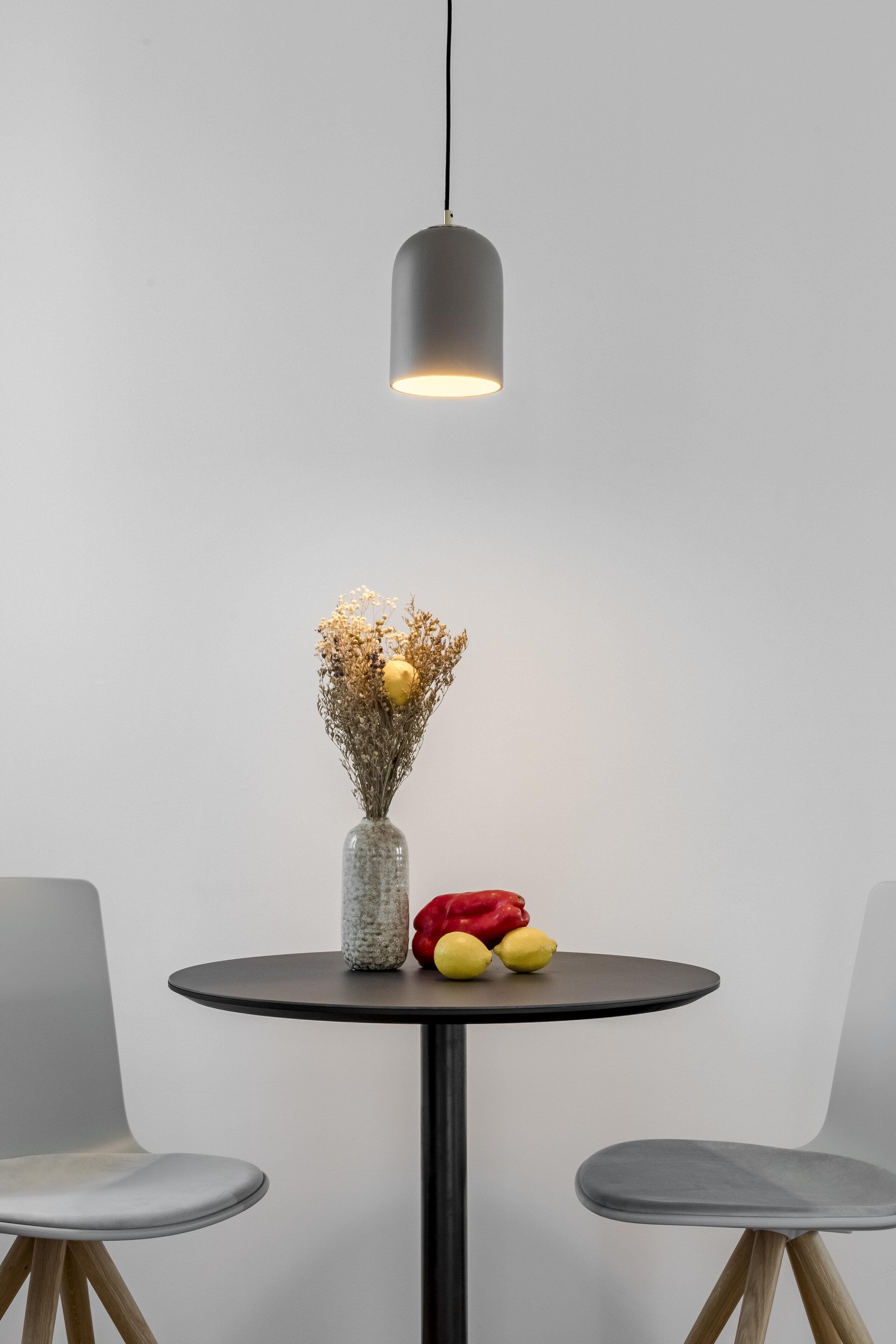 Una mesa redonda con un florero de flores secas y frutas, dos sillas y una lámpara colgante.