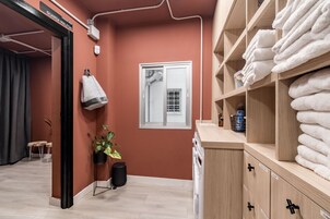 Ein Hotelzimmer mit roter Wand, einem Fenster mit Blick, einem Handtuchhalter, einer Pflanze und einem Holzschrank mit Handtüchern.