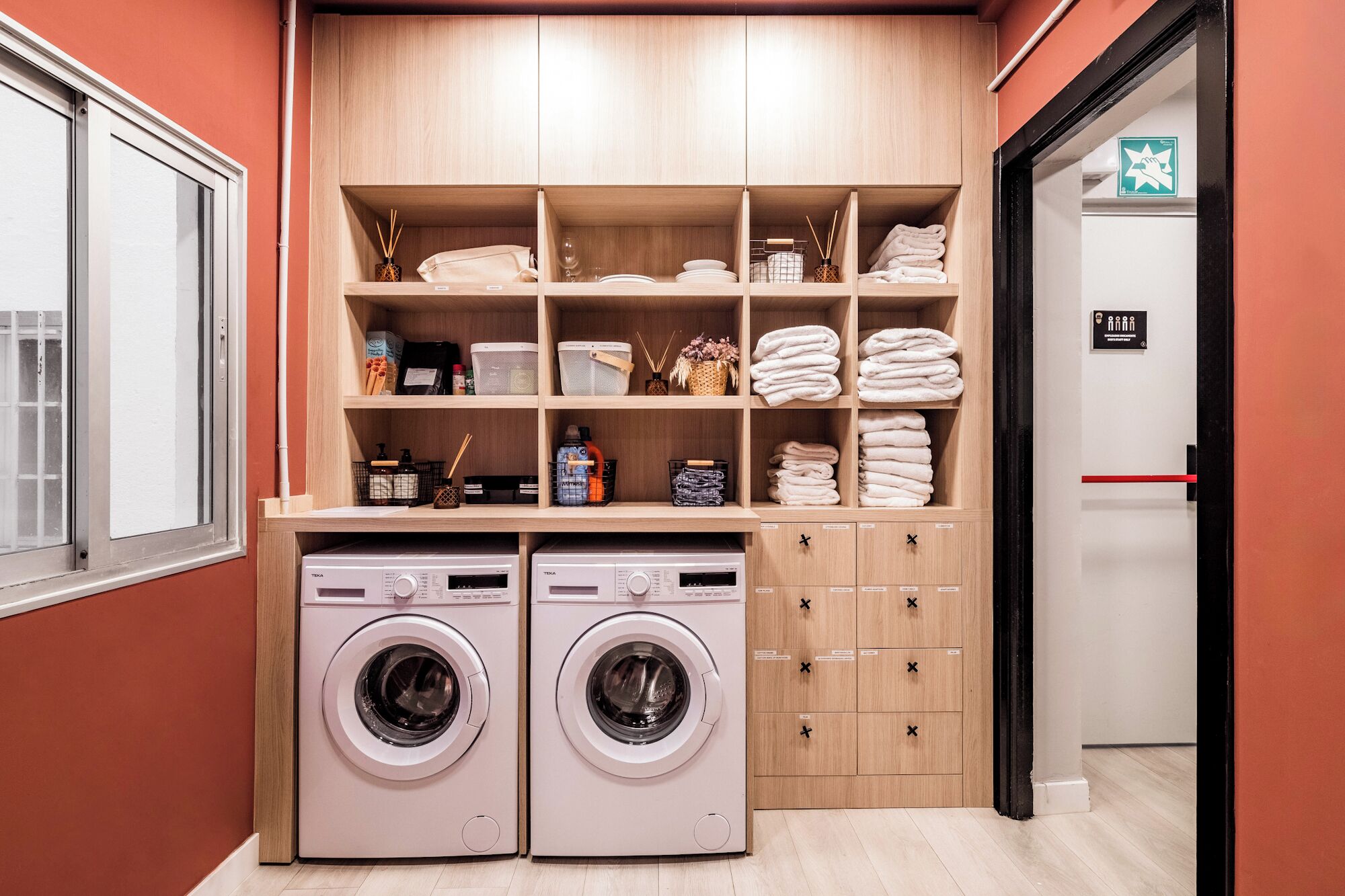 A laundry room with two washing machines, shelves with folded towels, and storage cabinets.