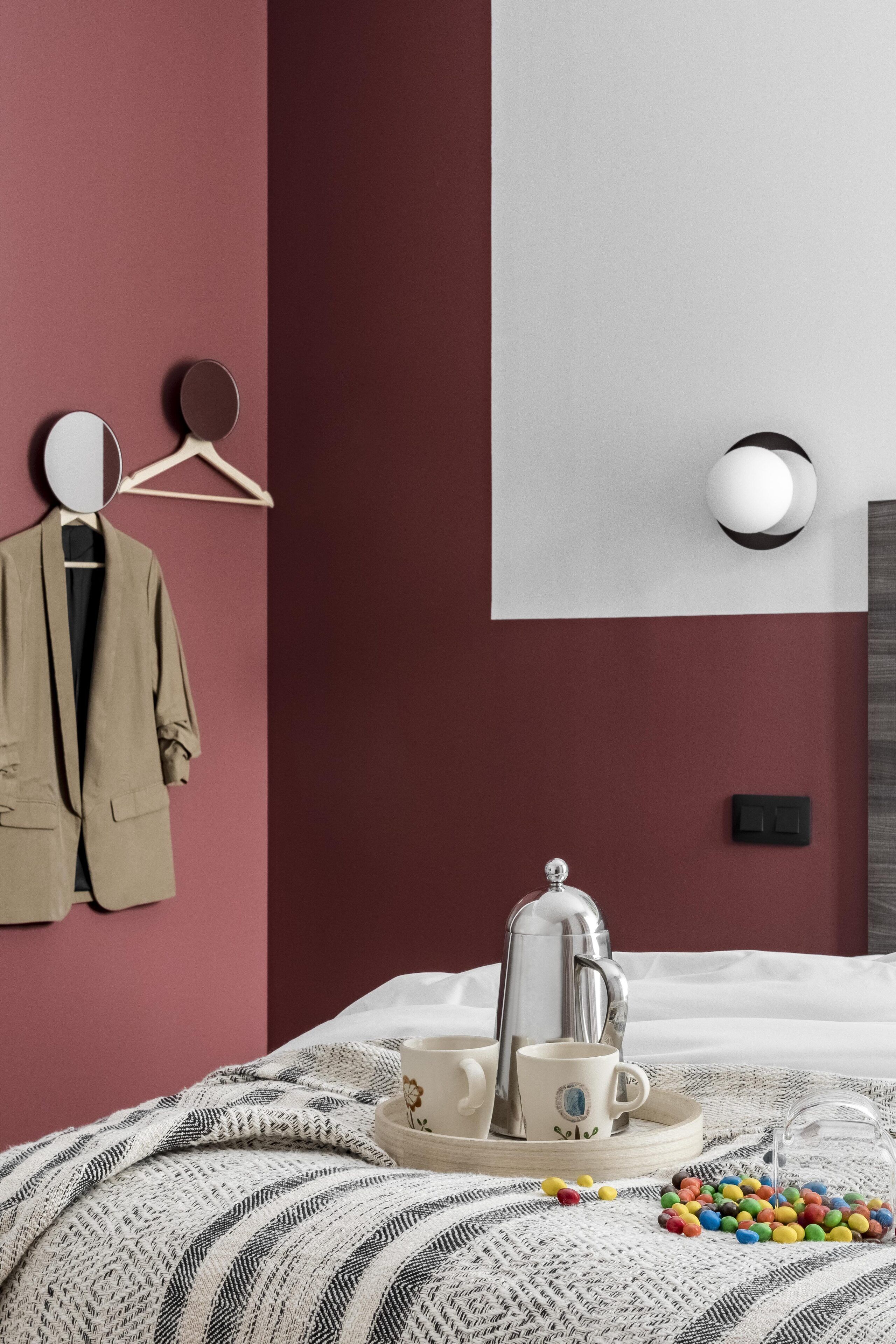 Un dormitorio ordenado con cama, perchero, cafetera, tazas y una bandeja con caramelos de colores.