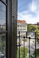 Blick aus einem Fenster mit Metallgitter auf eine Straße mit Gebäuden und Bäumen.