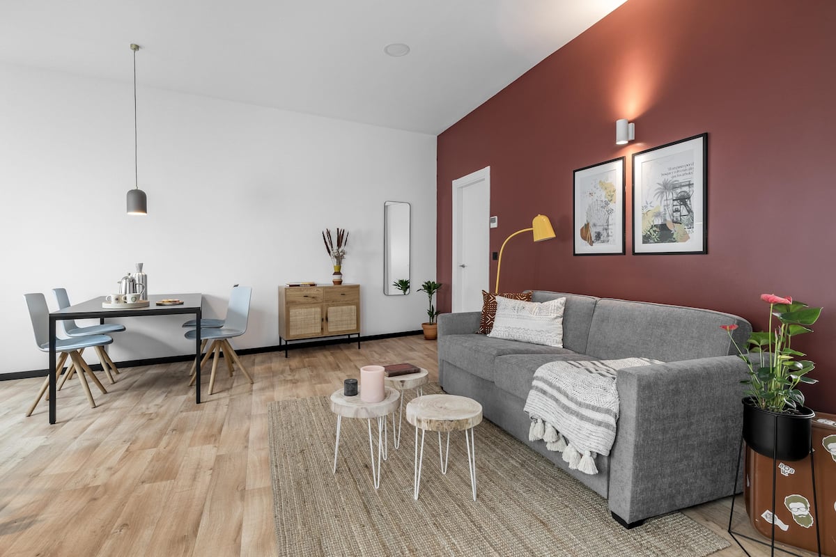 Una sala moderna con un sofá gris, una mesa de comedor con sillas, una mesa de centro y una mesita auxiliar.