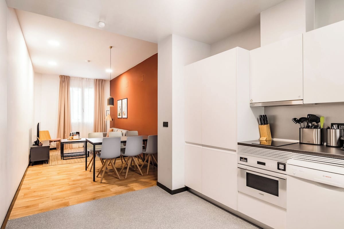 Una cocina moderna con armarios blancos, un horno Bosch y una zona de comedor con mesa y sillas.