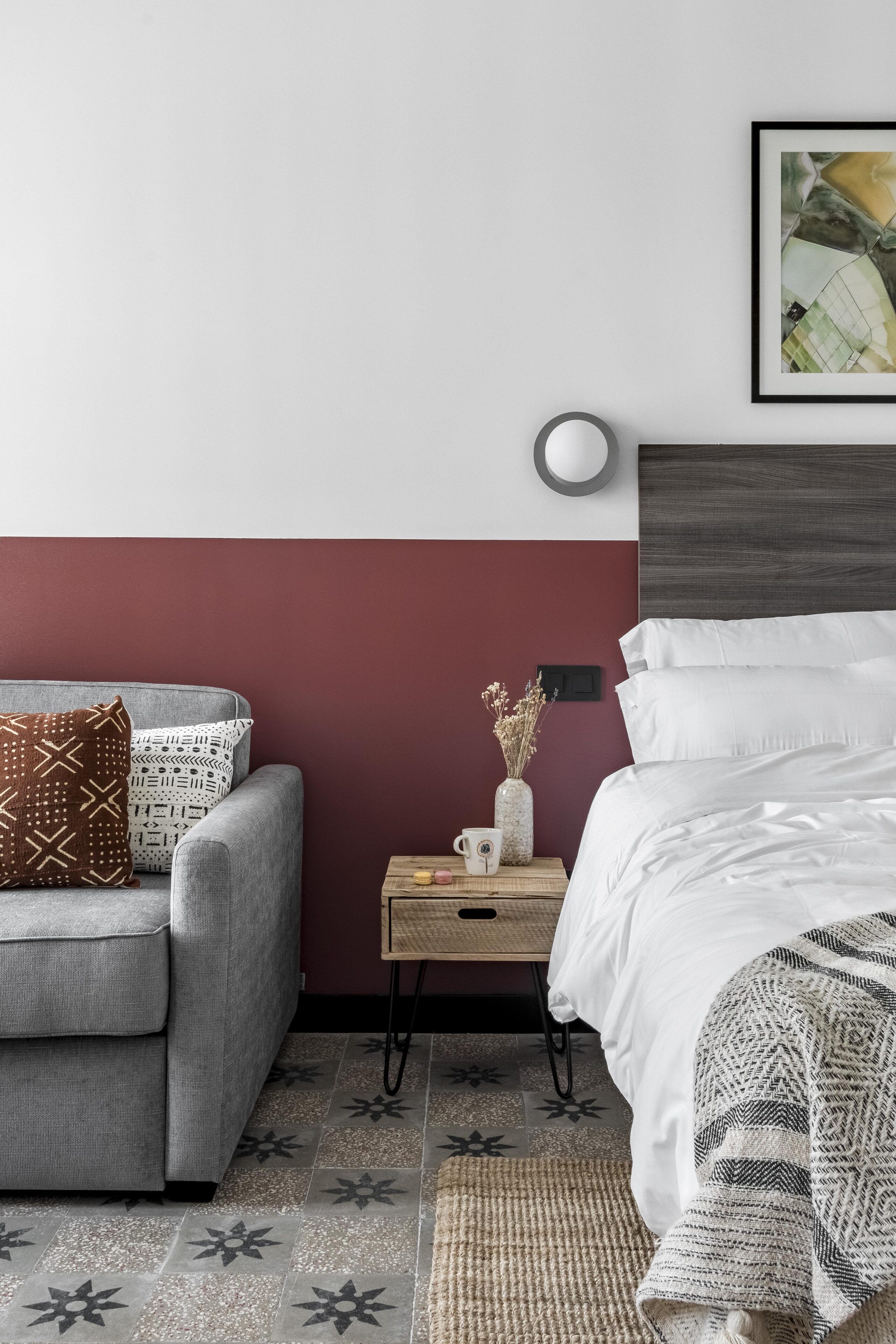 A bedroom with a grey sofa, a bedside table with a vase, and a bed with white bedding.