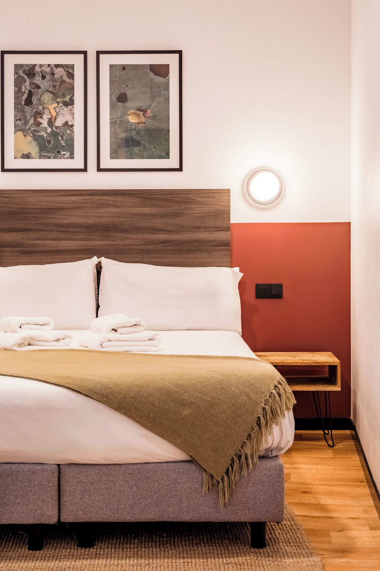 A neatly made bed with pillows and a blanket, a bedside table, and two framed abstract artworks on the wall.