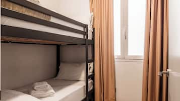 A bunk bed room with a wooden floor, a window with curtains, and a door.