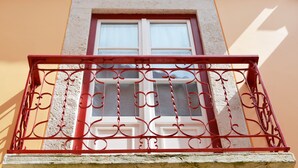 A balcony with ornate red metal railings and a white-framed window.