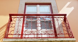 A balcony with ornate red metal railings and a white-framed window.